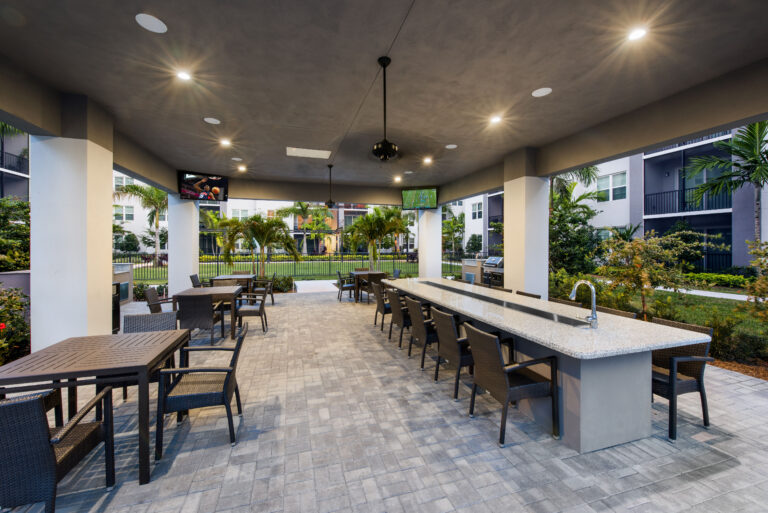 Outdoor covered dining area with televisions, tables and chairs at The Point at Palm Beach Grove